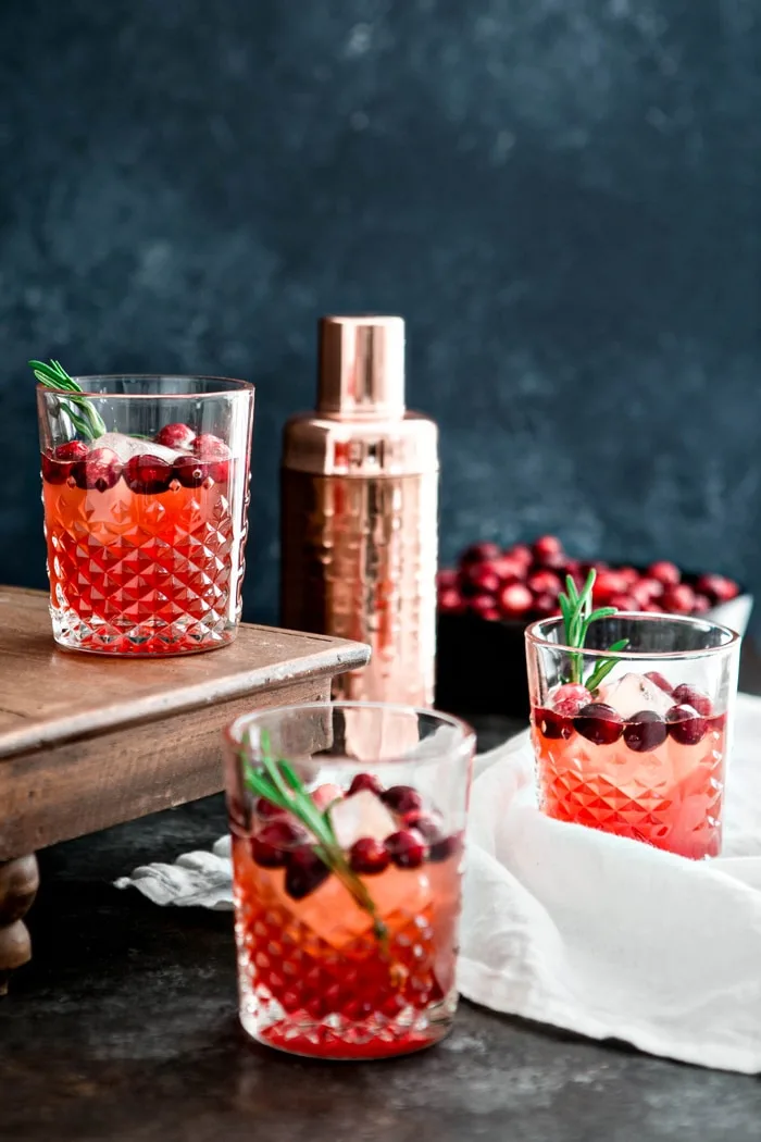 photo of 3 glasses of cranberry shrub cocktail on a dark background with a cocktail shaker