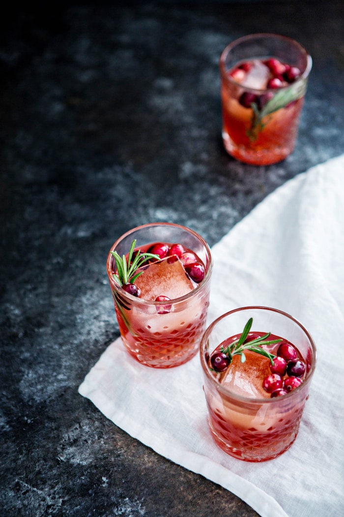 a table set with 3 cranberry shrub cocktails and rosemary sprigs