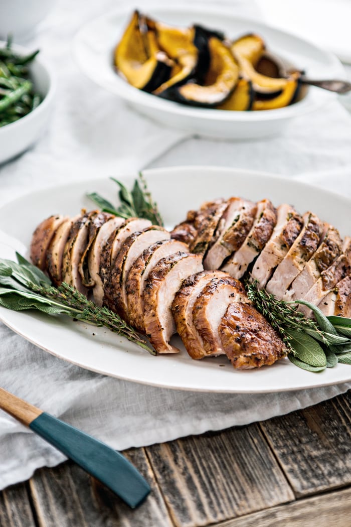 photo of a dry brine turkey on white platter with fresh herbs