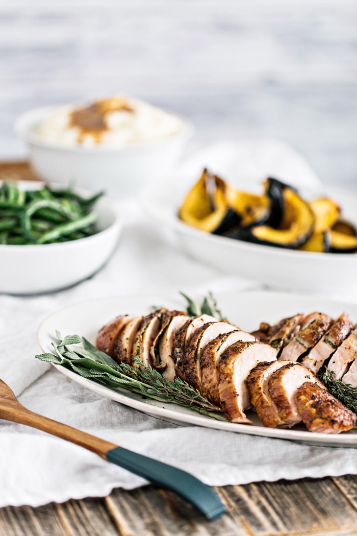 photo of a roasted dry brine turkey on white serving platter in front of green beans and roasted squash