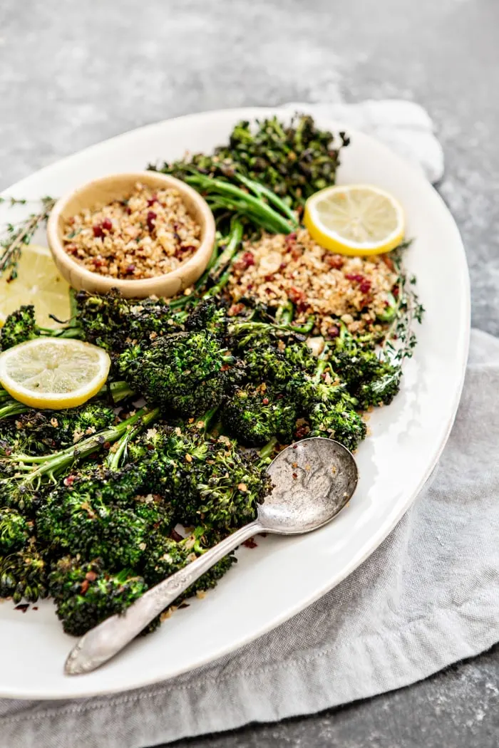 roasted broccolini on white serving platter with lemon slices and bread crumbs