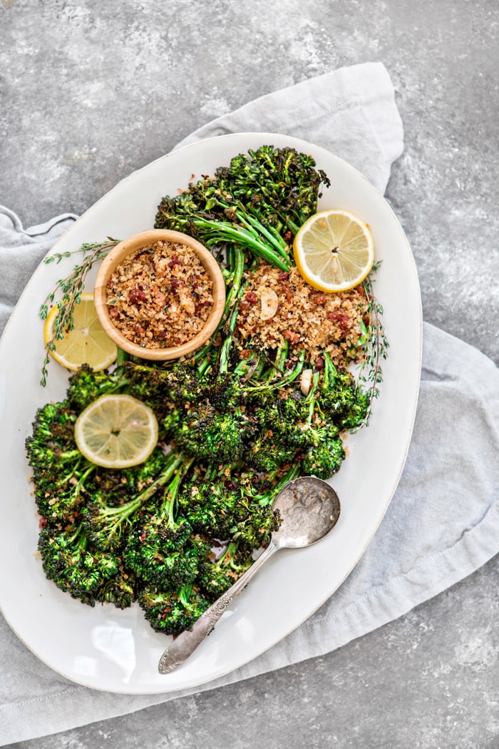 roasted broccolini on a white serving platter with lemon slices and panko bread crumbs