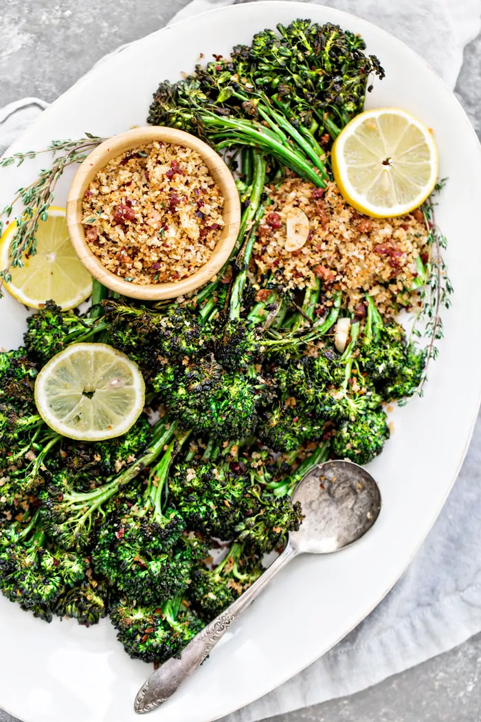 roasted broccolini with lemon slices, bread crumbs, and spoon on white serving platter