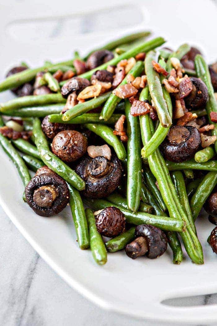 sauteed green beans with bacon, garlic, and balsamic mushrooms on white platter
