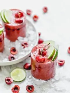 Cherry Limeade Slush in a clear glass surrounded by ice with fresh limes and cherries