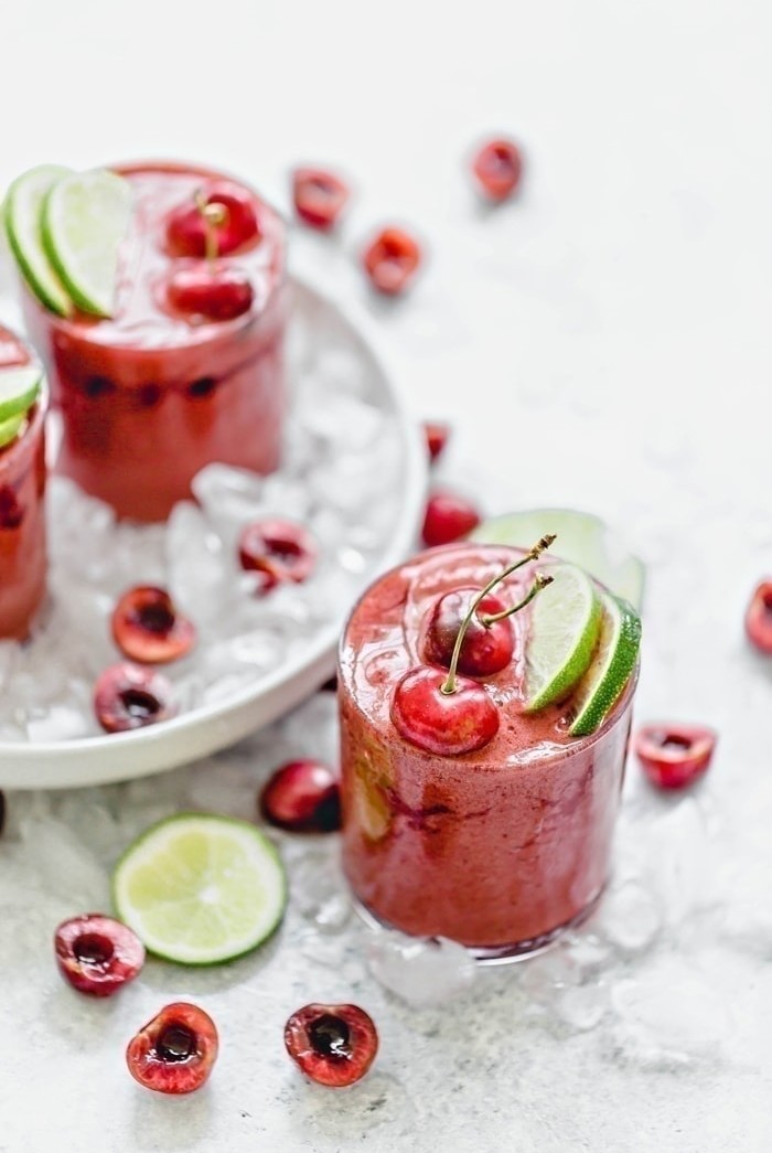 Cherry Limeade Slush in a clear glass surrounded by ice with fresh limes and cherries