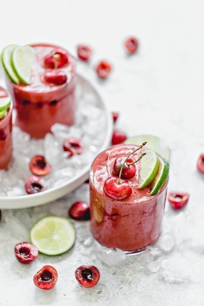 Cherry Limeade Slush in a clear glass surrounded by ice with fresh limes and cherries