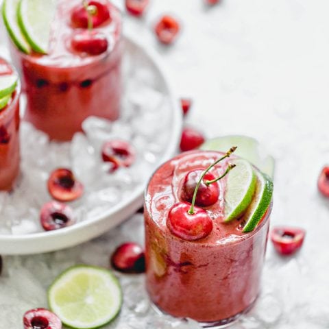 Cherry Limeade SLushie in a glass with ice and fresh cherries