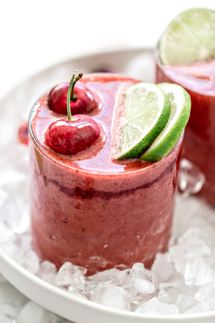 close up cherry slushie in a clear glass with fresh cherries and limes