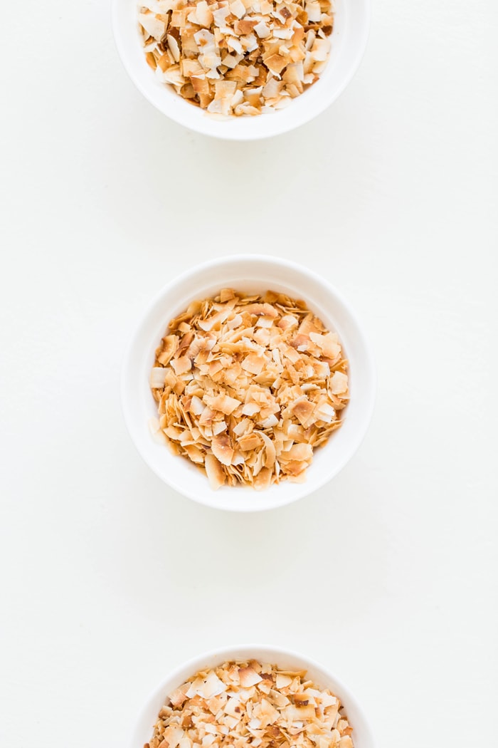 3 white bowls of toasted coconut on white background