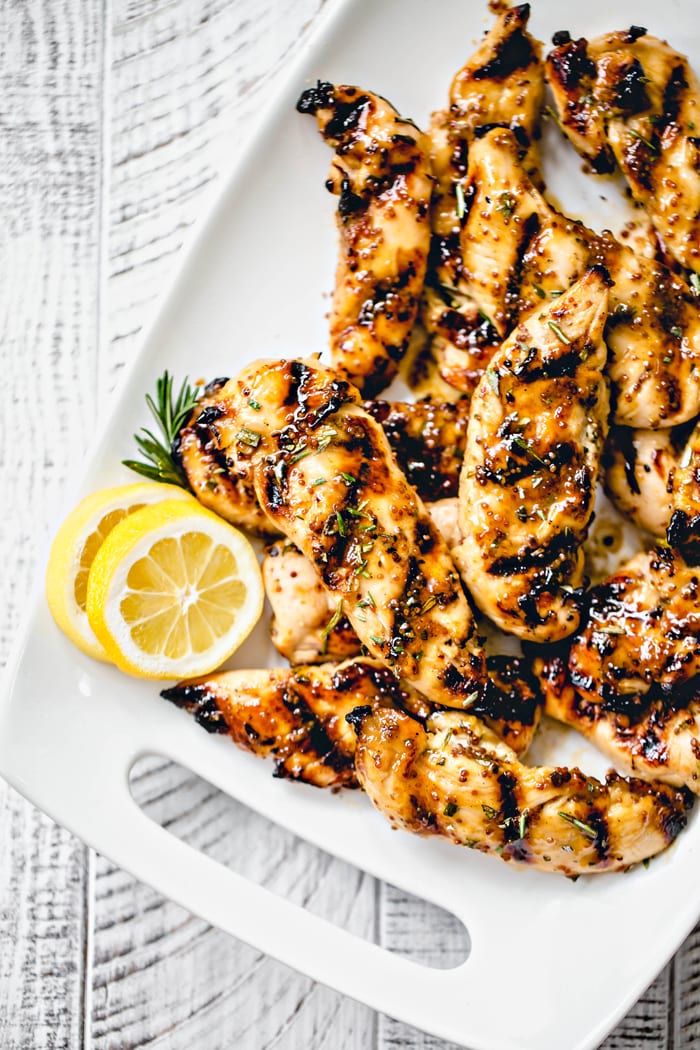 overhead image of grilled chicken with lemon slices on a white background