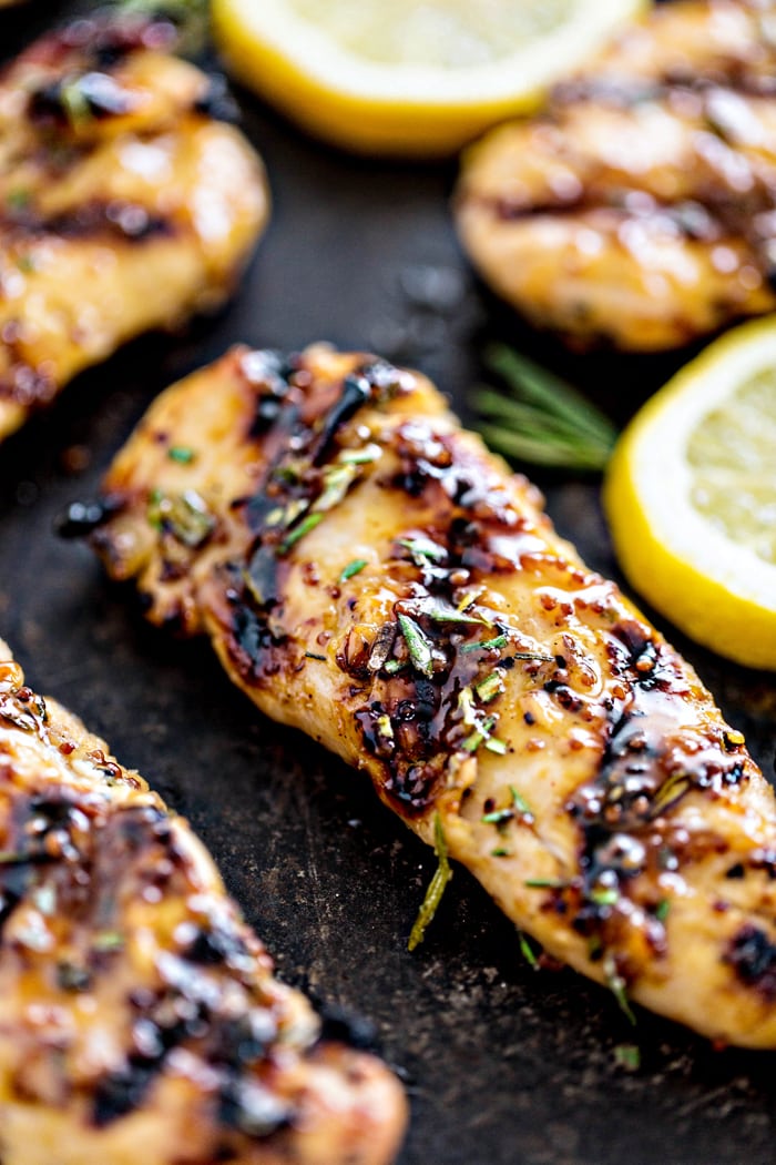 grilled chicken tenderloins on a black background with a lemon slice