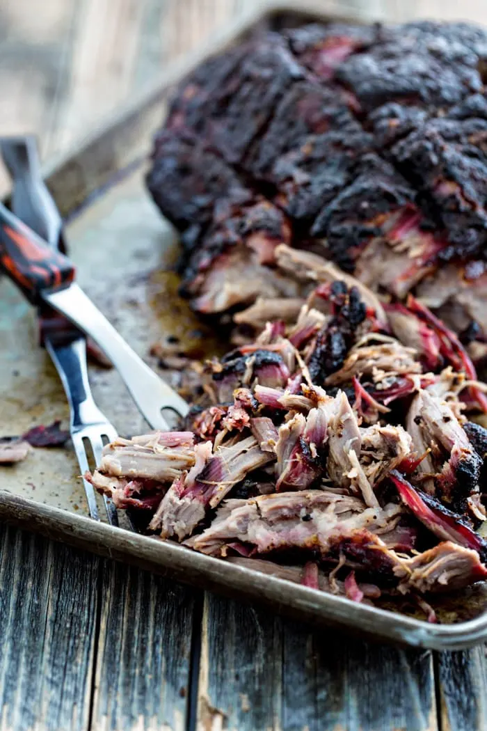 photo of a smoked pork shoulder on a baking sheet with shredded smoked pulled pork