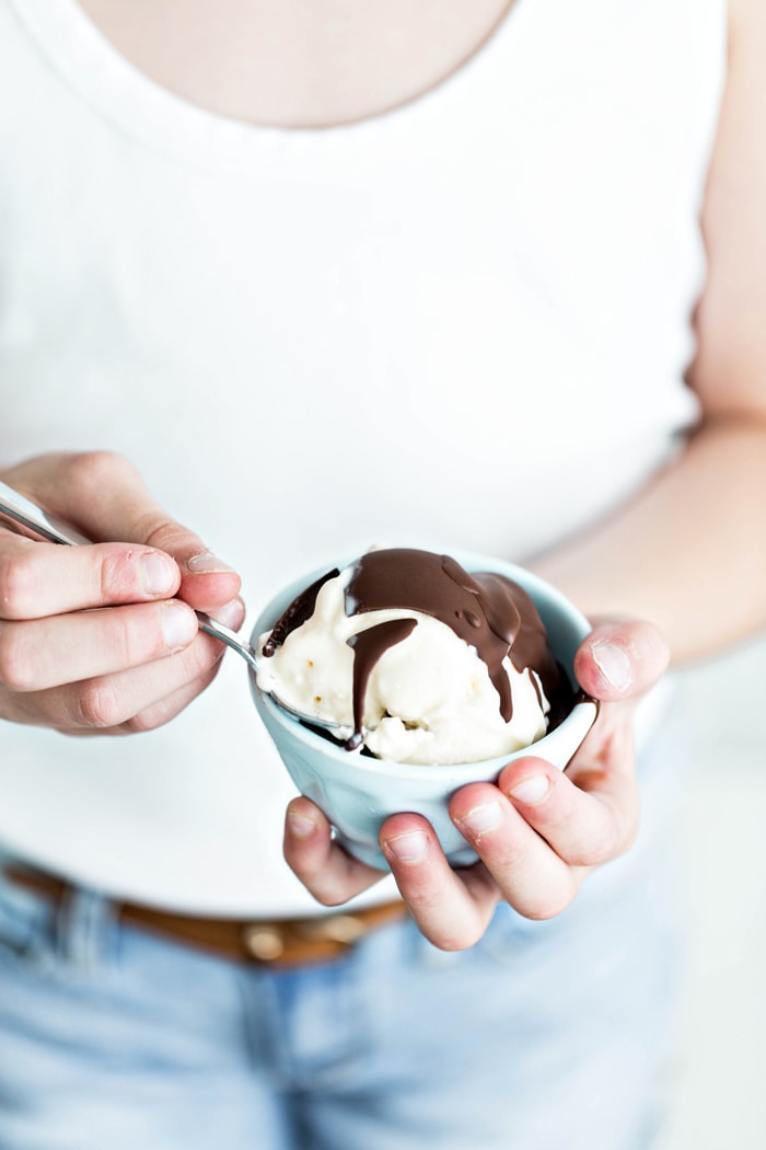 girl in white shirt holding a bowl of ice cream with chocolate topping