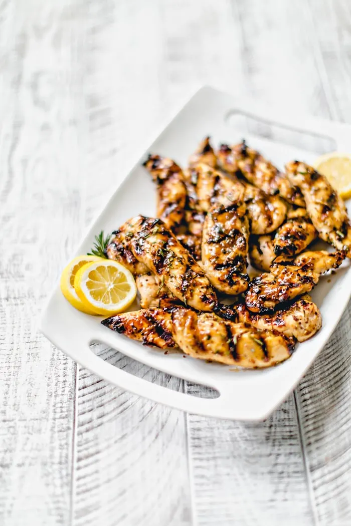 white platter with grilled glazed chicken tenderloins and lemon slices