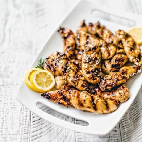 grilled chicken with lemon slices on a white platter and white background