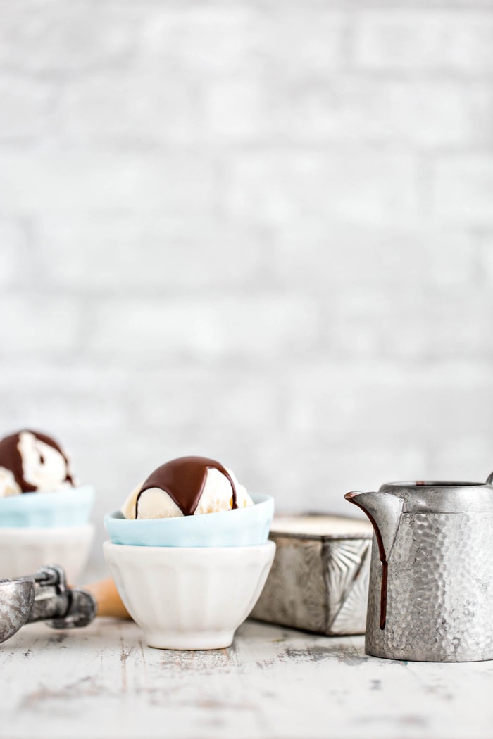 two bowls of vanilla ice cream with homemade magic shell recipe in front of a grey brick wall