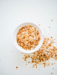 overhead shot of a white bowl of toasted coconut on a white background