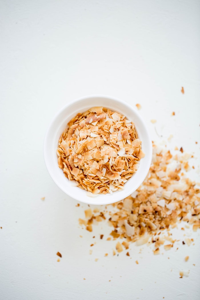 overhead shot of a white bowl of toasted coconut on a white background