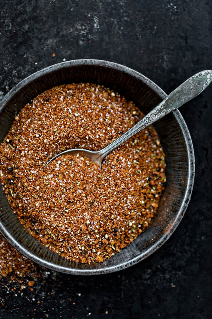 overhead image of bowl of pork rub seasoning with spoon on a dark background