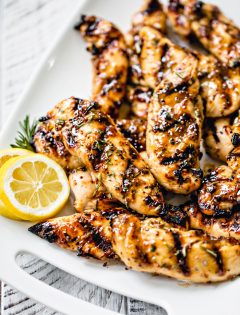close up photo of grilled chicken tenderloins on a white platter