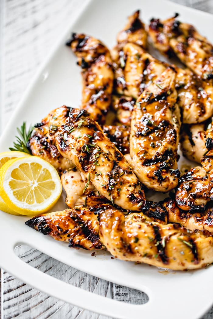 close up photo of grilled chicken tenderloins on a white platter