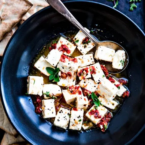 black bowl with marinated feta surrounded by pita chips