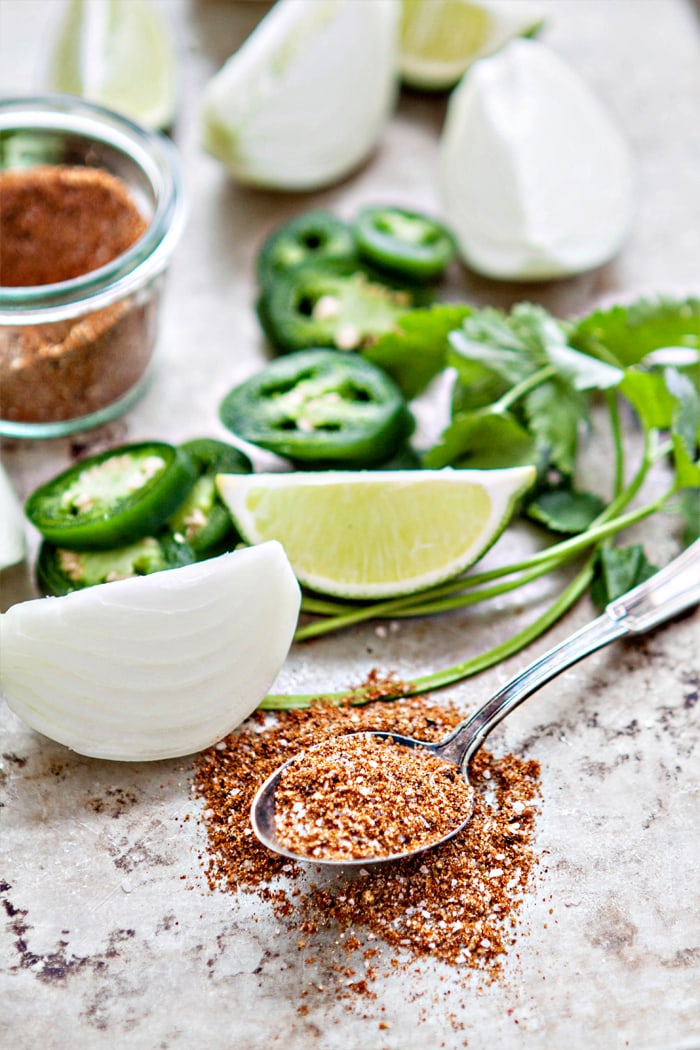 onion, lime, and cilantro on a sheet pan with spoon of seasoning