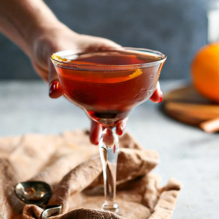 photo of a woman holding a black manhattan cocktail in a coupe glass