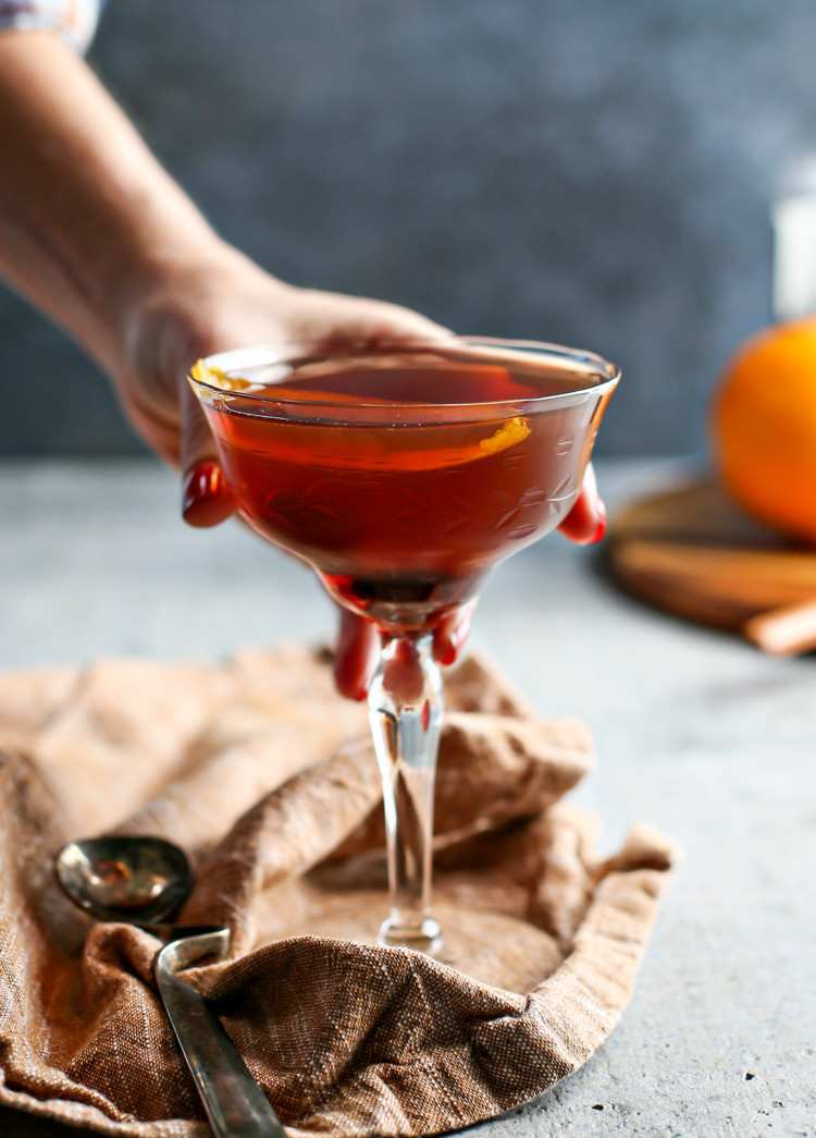 photo of a woman holding a black manhattan cocktail in a coupe glass
