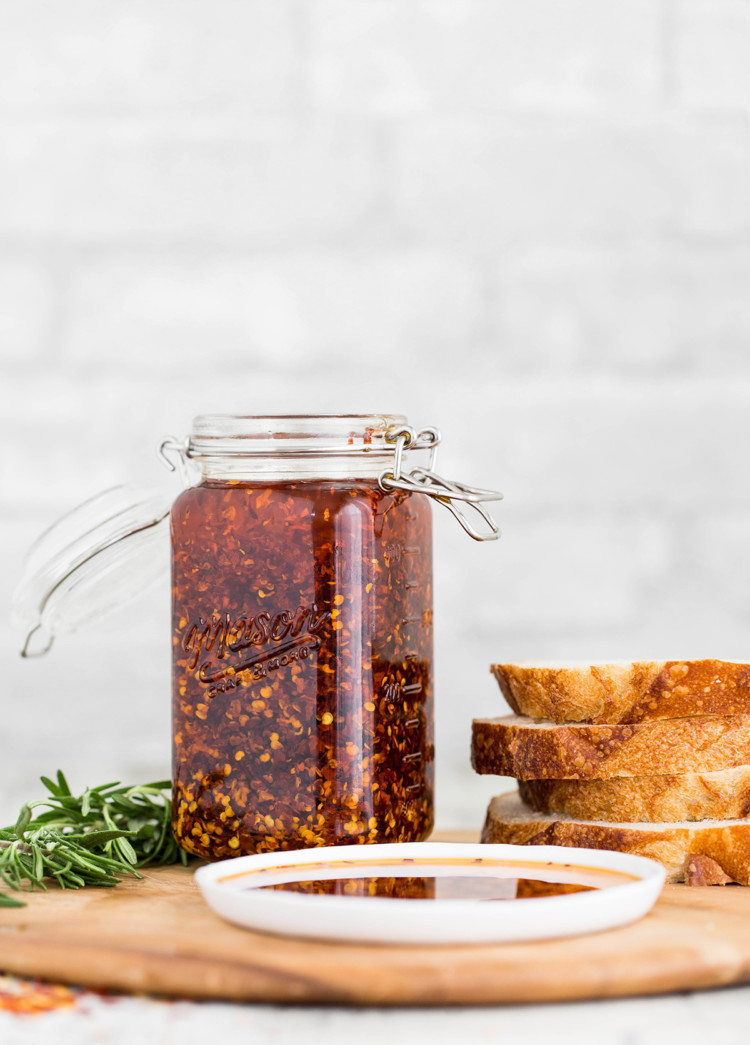 chili garlic oil in a jar next to sliced artisan bread and fresh rosemary