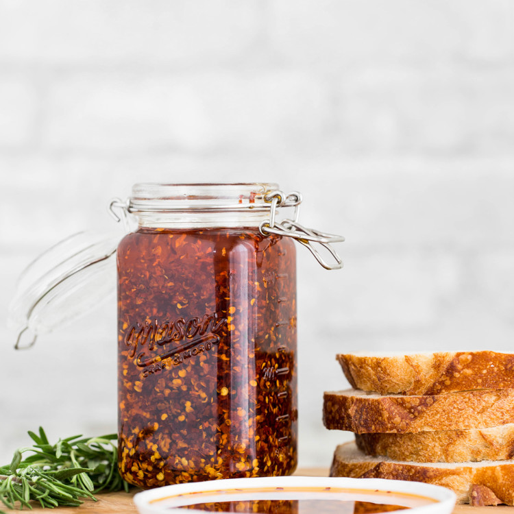 chili garlic oil in a jar next to sliced artisan bread and fresh rosemary