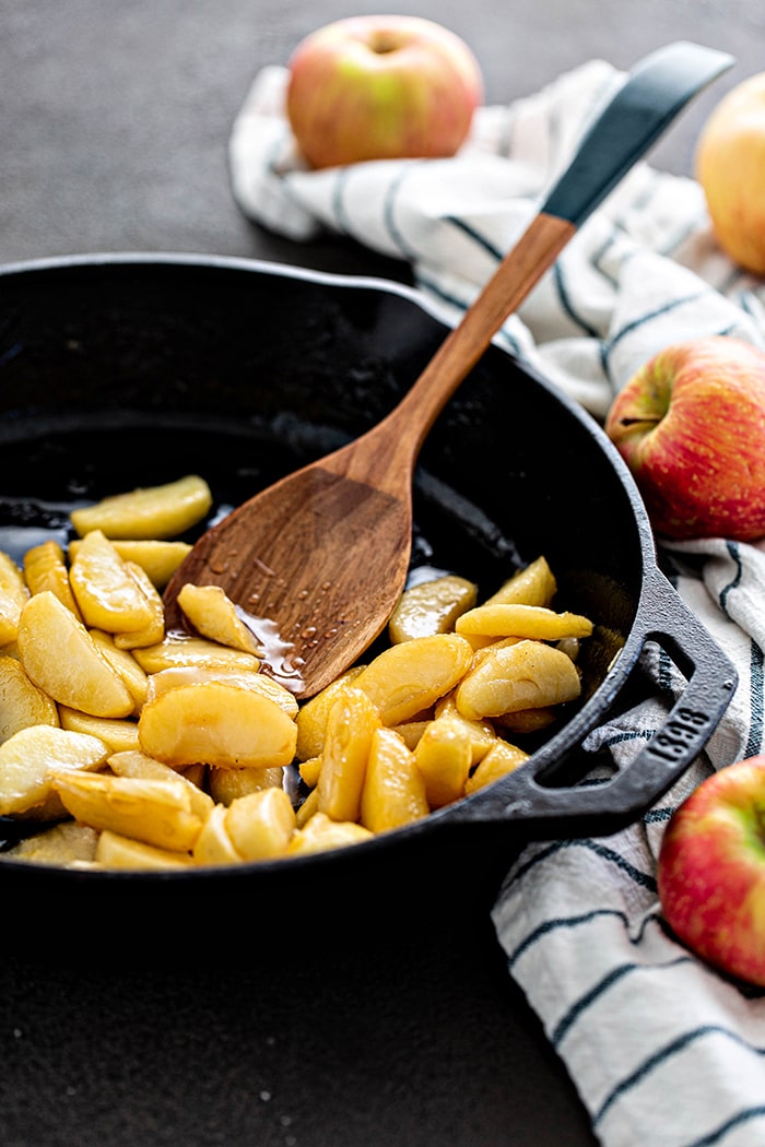 caramelized apples in a cast iron pan with wooden spoon