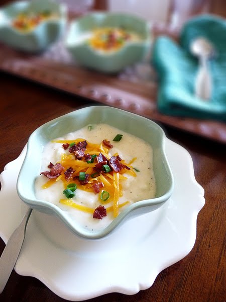 A bowl of cheddar baked potato soup garnished with bacon, cheese, and green onions. 