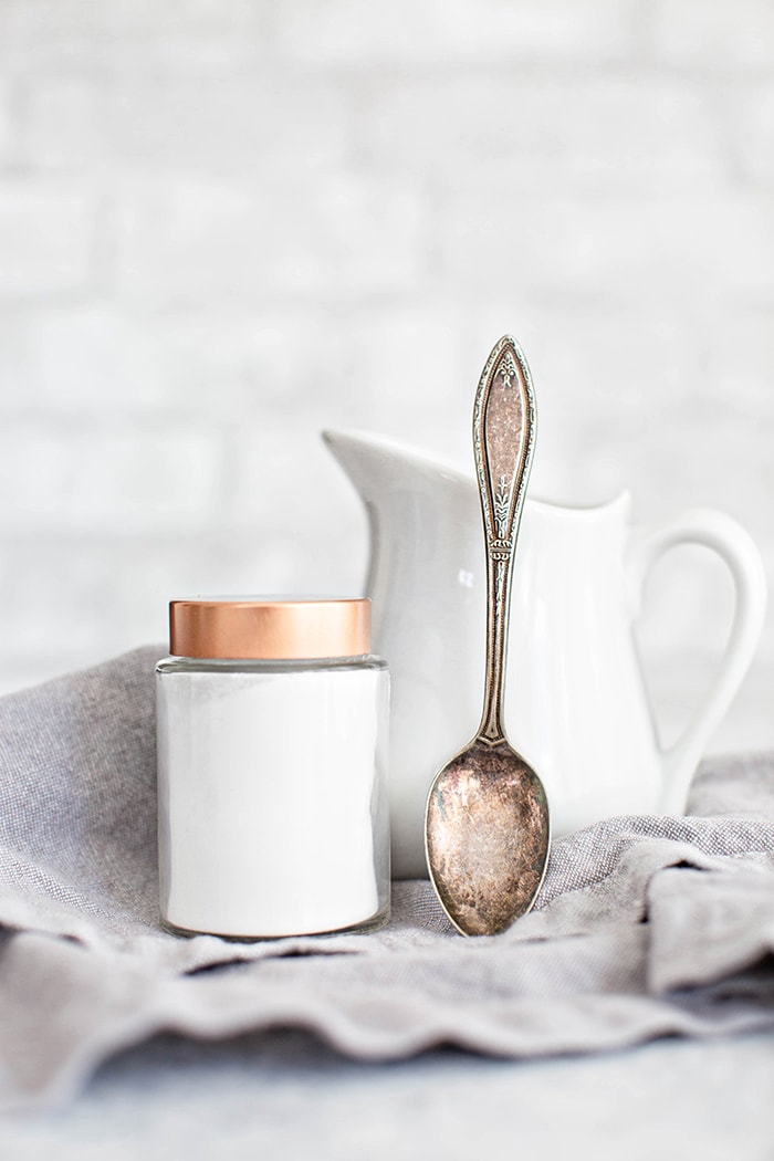 A jar of cream of tartar with a spoon next to a small white pitcher of milk, ready to be used as a buttermilk substitute.