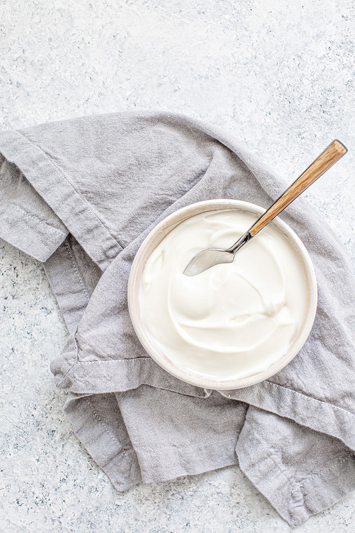 A jar of sour cream with a spoon standing up against it, a rich and tangy buttermilk substitute for baked goods and dressings.