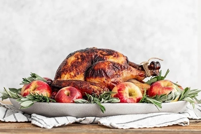photo of an apple cider turkey brined turkey on a platter with apples and sage