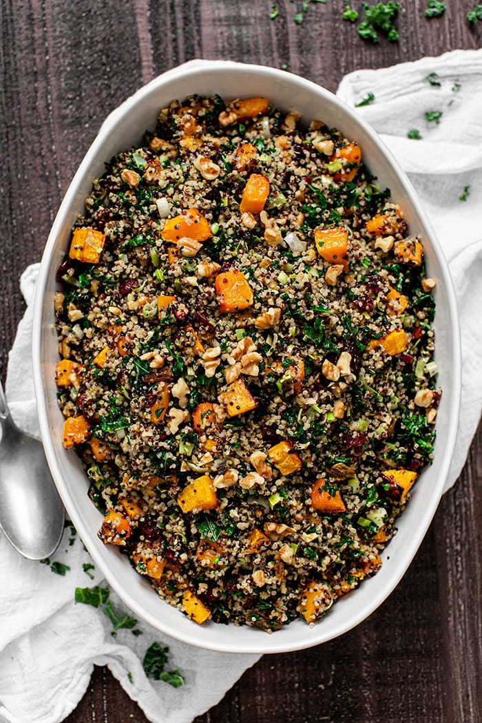 overhead photo of a bowl of butternut squash stuffing (a healthy stuffing recipe) set on a dark table with a white table cloth and serving spoon