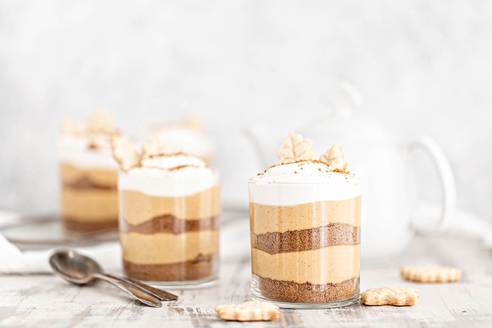 four no bake pumpkin cheesecakes served in jars on a white wooden table with spoons