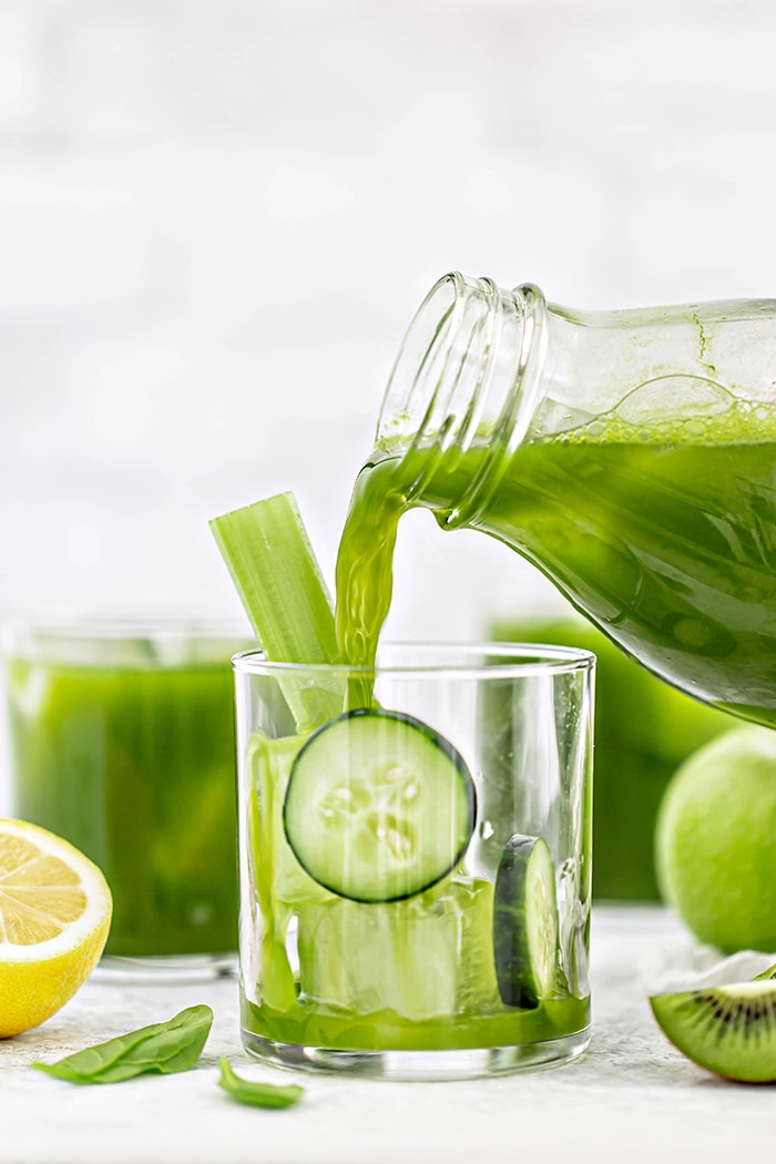 green juice pouring into a glass with cucumber slices and ice cubes