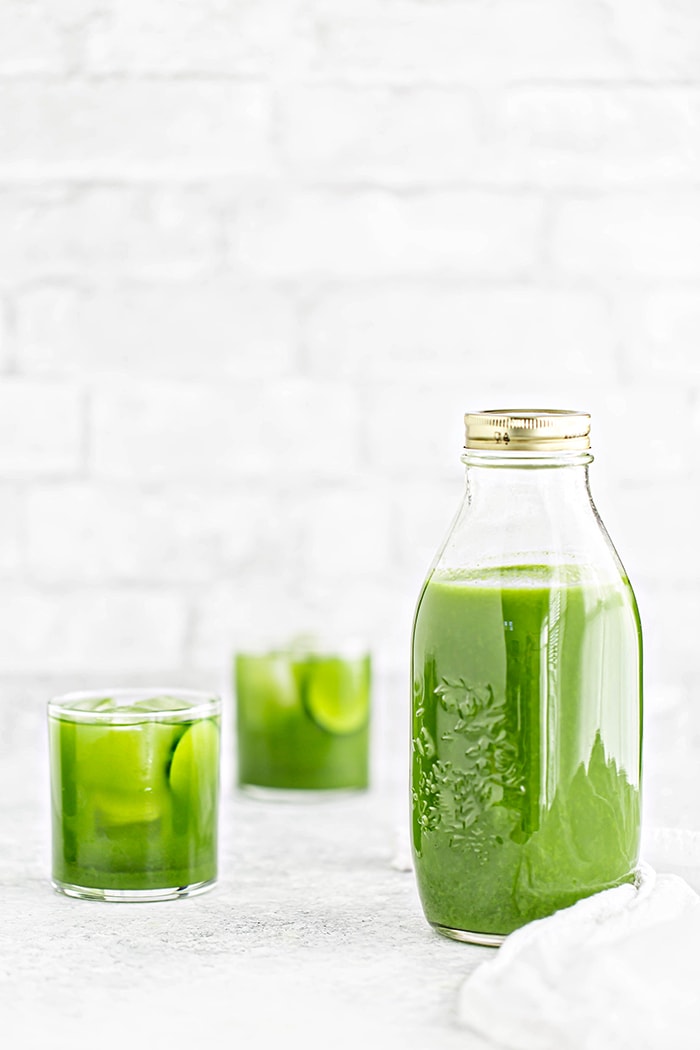 a jar of green juice and two glasses with ice and green juice