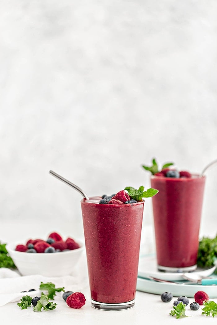 glass with berry mango kale smoothie and straw