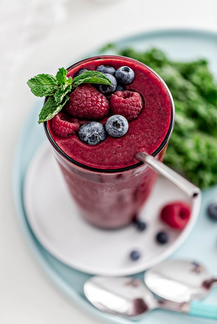 glass with berry mango kale smoothie and straw