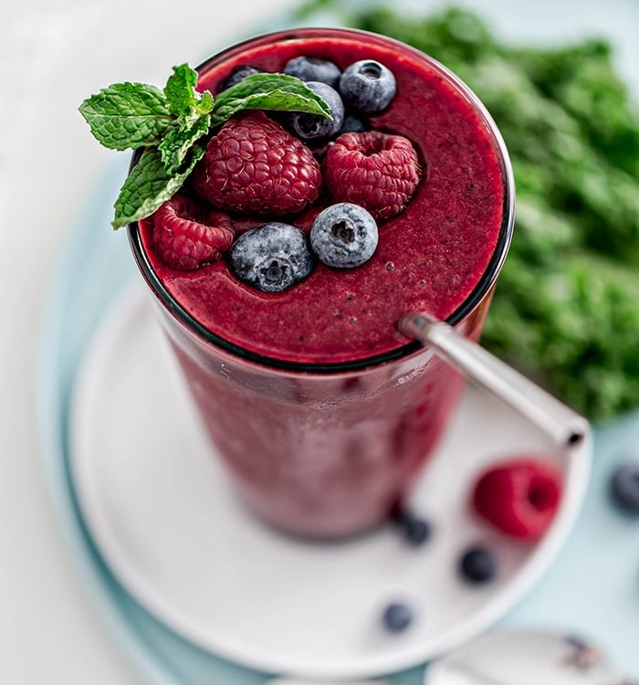 glass with berry mango kale smoothie and straw