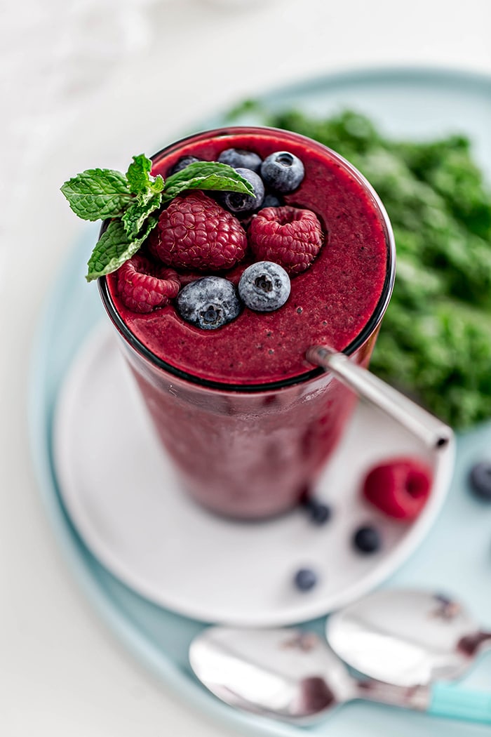 glass with berry mango kale smoothie and straw