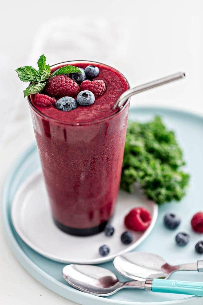 glass with berry mango kale smoothie and straw