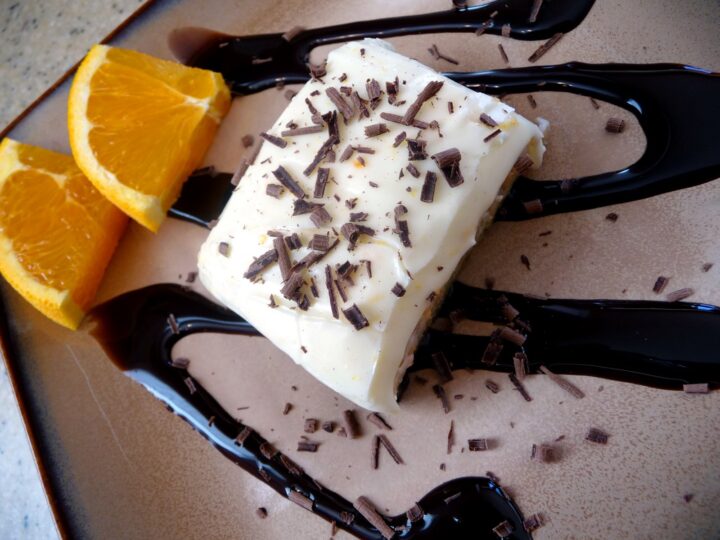 Overhead view of a frosted orange brownie drizzled with chocolate sauce. 