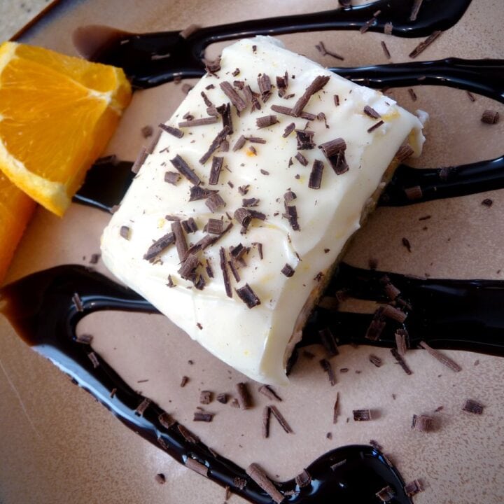 Overhead view of a frosted orange brownie drizzled with chocolate sauce.