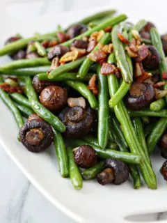 sauteed green beans with bacon on a white plate on a white marble counter