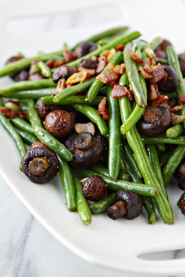 sauteed green beans with bacon on a white plate on a white marble counter
